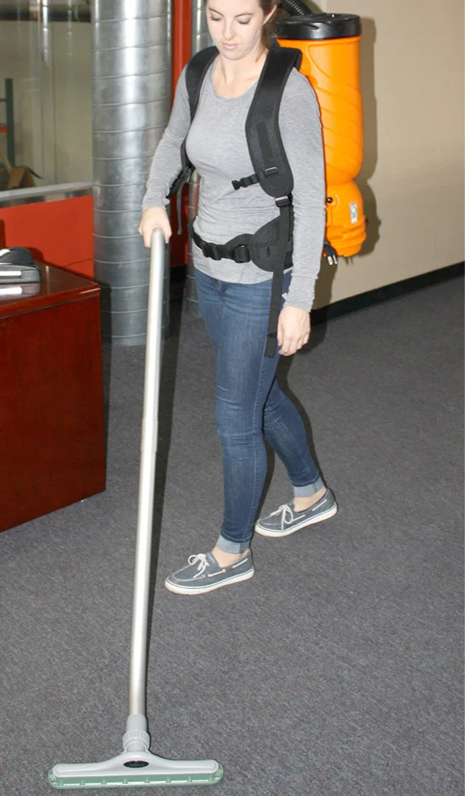 Person using a backpack vacuum cleaner on a carpeted floor.